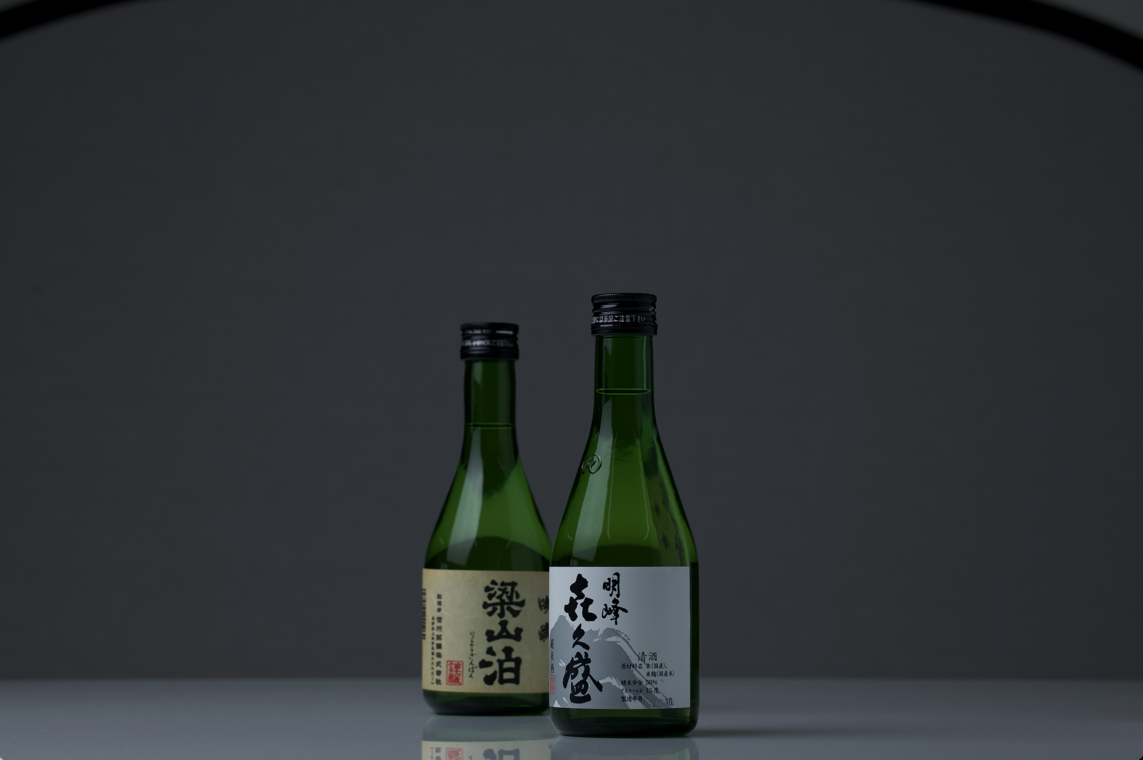 Two green sake bottles photographed in low studio light