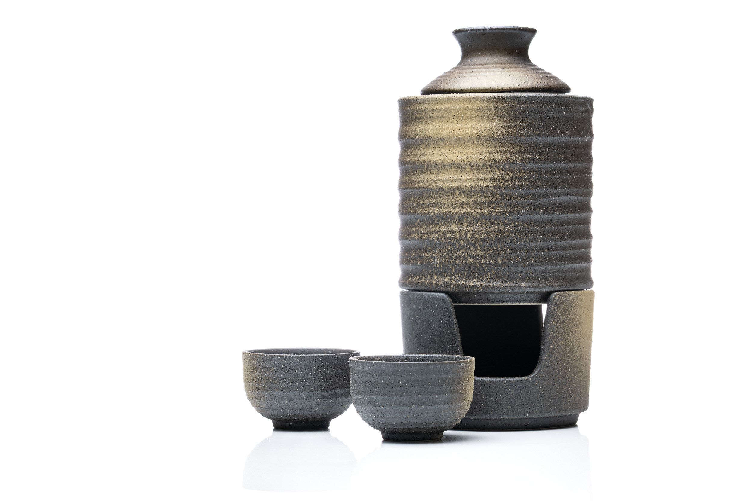 Dark stoneware sake set with two cups on a bright reflective surface